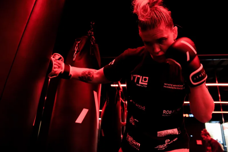 Boxer working a punch bag under red lighting