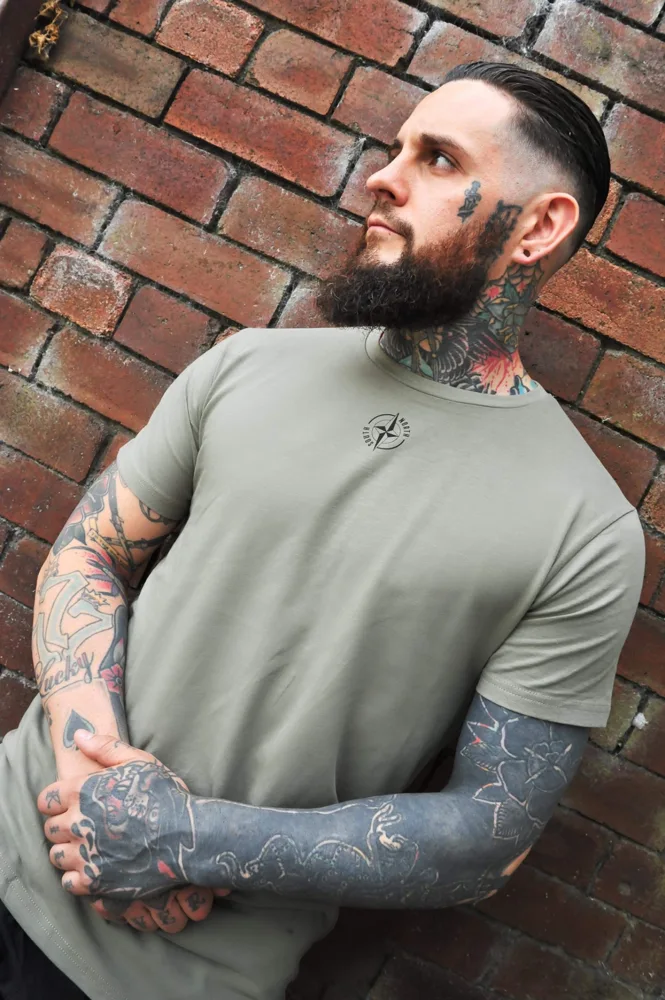 Model showcasing a muted green T-shirt against brickwork