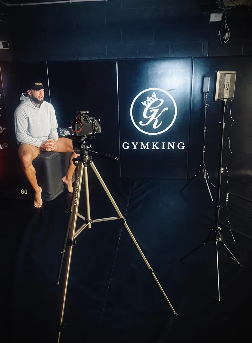 Behind the scenes of an interview shoot, with a camera on a tripod and studio lighting in a gym