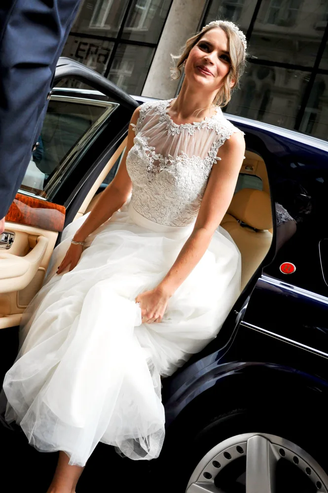 Bride seated beside the open door of a wedding car